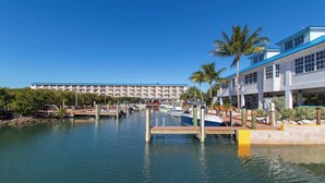 A marina with boats docked, a building with multiple floors, and palm trees.