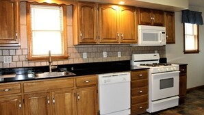 A kitchen with wooden cabinets, a microwave, a dishwasher, and a stove. - Cooperstown Baseball Rentals - Sky Box (Oneonta)