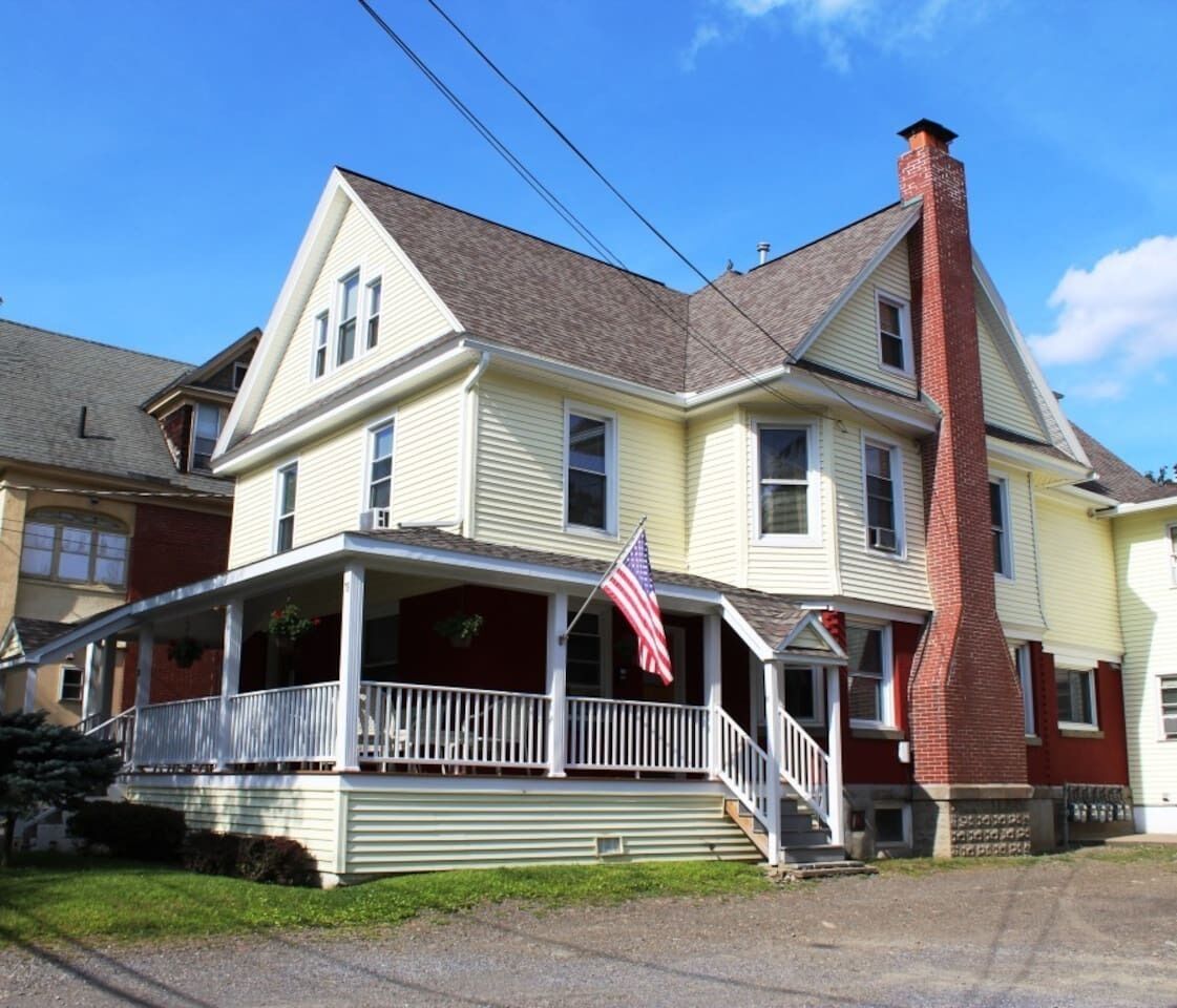 A two-story house with a porch, a chimney, and an American flag.