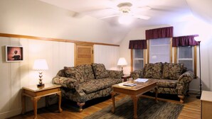 A living room with two floral-patterned sofas, a wooden coffee table, and two lamps on side tables. - Cooperstown Baseball Rentals - Sky Box (Oneonta)