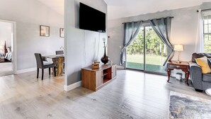 A spacious living room with a flat-screen TV mounted on the wall, a dining area with a table and chairs, and a large window with curtains. - Port Charlotte Home Near Beaches & Dining (Port Charlotte)