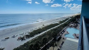 A beach view from a balcony with a pool and lounge area.