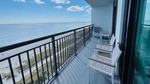 A balcony with a view of the ocean, equipped with white chairs and a glass railing.
