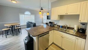 Eine moderne Küche mit weißen Schränken, einer Granitabdeckung und einem Geschirrspüler. Es gibt eine Essecke mit Tisch und Stühlen.