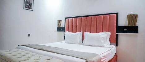 A neatly arranged bedroom with a bed, a bedside table, a wall-mounted air conditioner, and a framed picture on the wall.