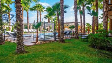 Un espace aménagé au bord de la piscine, avec des chaises longues et des parasols, entouré de palmiers.