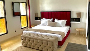A modern bedroom with a large bed, a tufted headboard, a bedside table, a small stool, and a large window. - 
luxury Villa Marrakech  (Marrakech)
