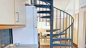 Eine Küche mit Herd, Spüle und einer blauen Wendeltreppe, die in einen Essbereich mit Tisch und Stühlen führt.