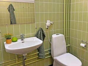 Ein Badezimmer mit einem weißen Waschbecken, einer Toilette und einem Spiegel. Ein Handtuch hängt an der Wand und auf dem Waschbecken steht eine kleine Pflanze.