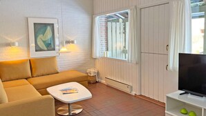 Ein Wohnzimmer mit einer Couch, einem Couchtisch, einer TV-Konsole und einem Fenster mit Vorhängen.