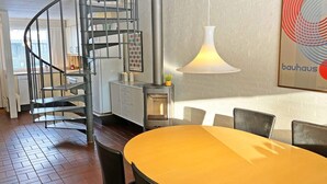 Eine moderne Küche mit Wendeltreppe, einem Essbereich mit gelbem Tisch und einem Bauhaus-Poster an der Wand.