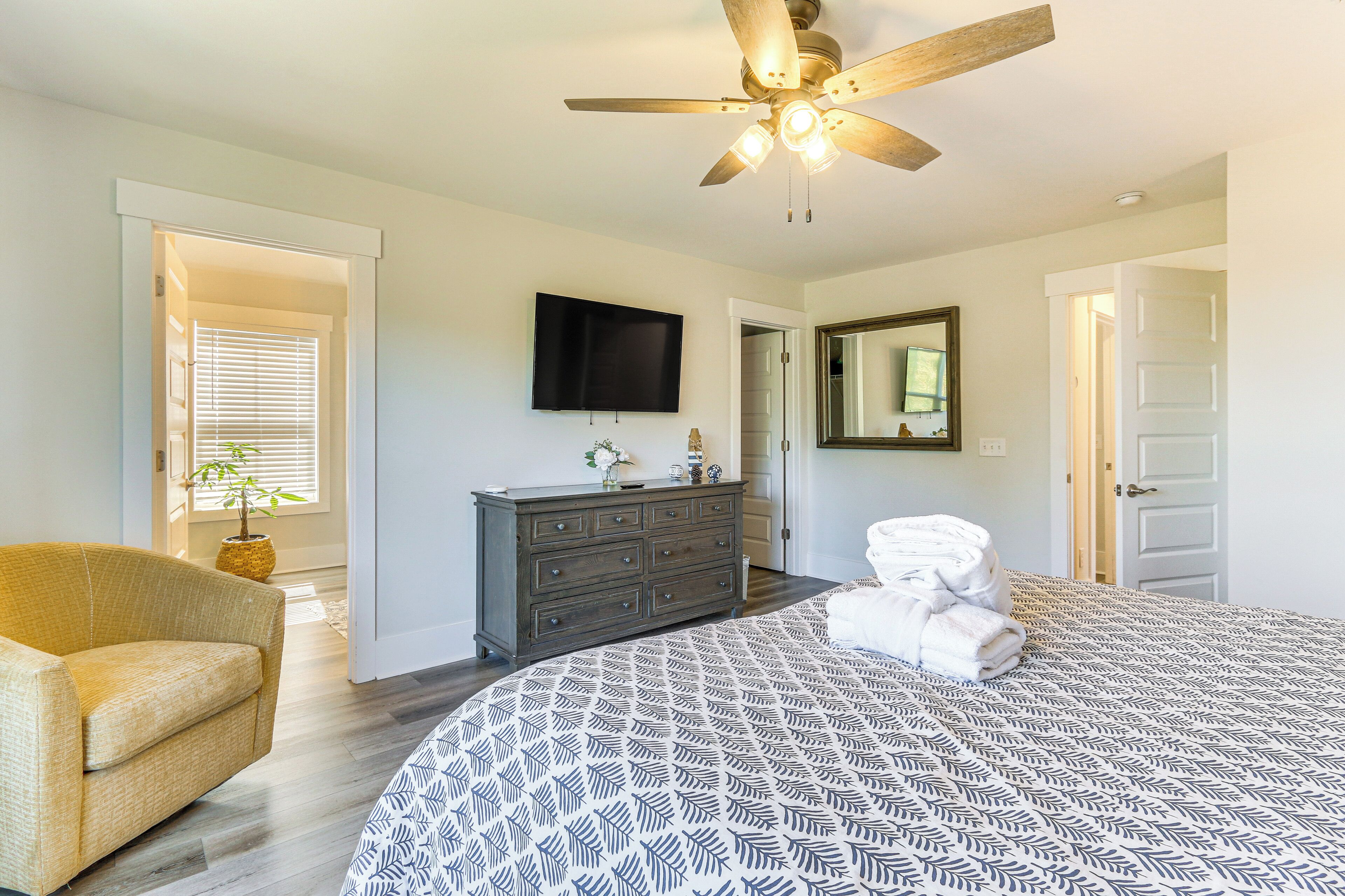 A bedroom with a large bed, a dresser, a television, and a ceiling fan.