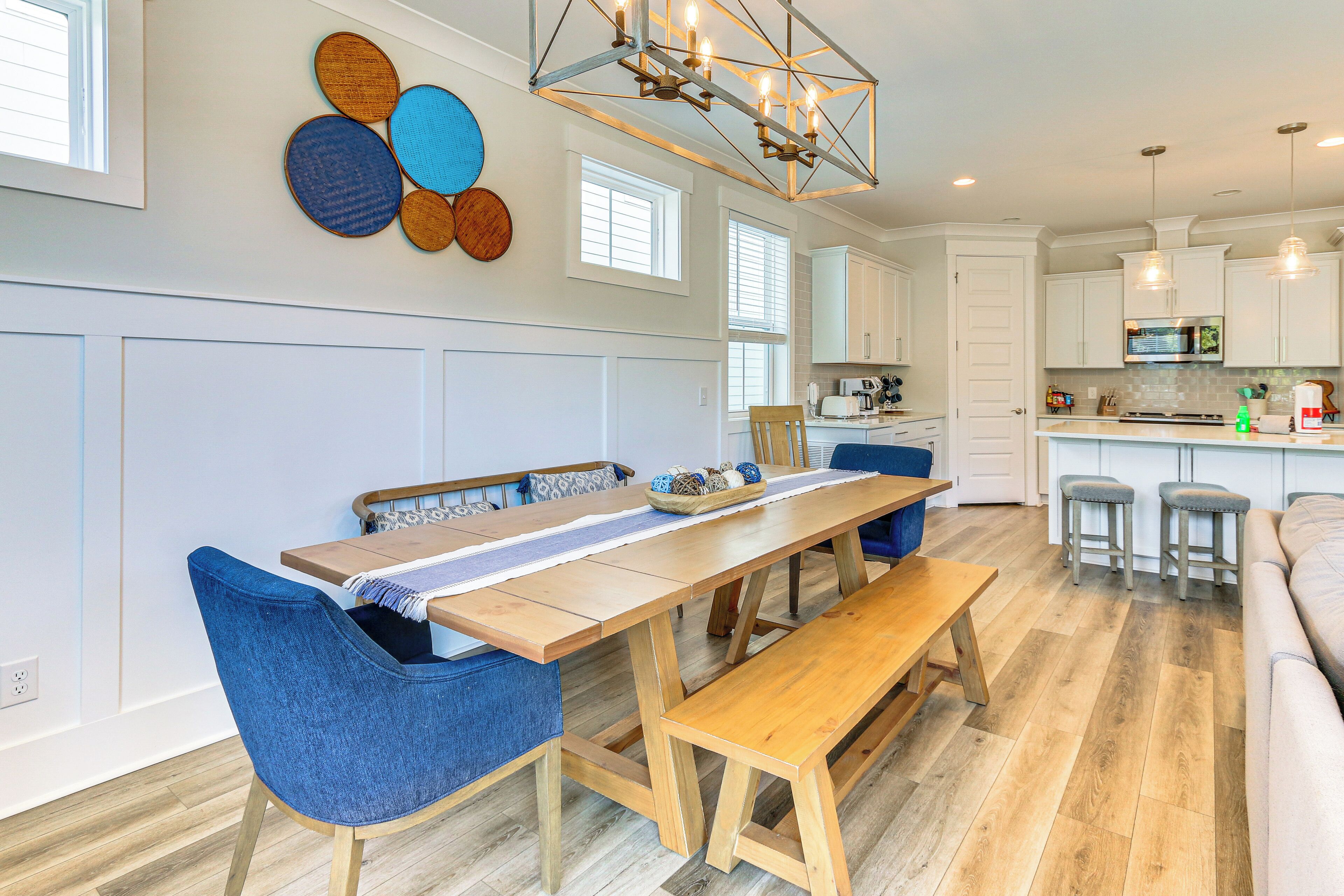 Een moderne keuken met witte kastjes, een houten eettafel met blauwe stoelen en een hanglamp.