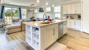 A spacious kitchen with white cabinetry, a central island with a sink, and a dining area with a sofa and table. - 1 Mi to Beach: Family-friendly Hilton Head Retreat (Hilton Head Island)