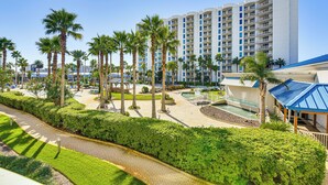 A hotel with a modern design, featuring a central courtyard with palm trees, a swimming pool, and a covered area with a blue roof. - Walk to Beaches: Resort Condo in Destin! (Destin)