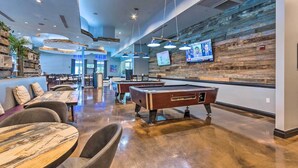 A billiards room with tables and chairs, a pool table, and a wooden wall with a TV. - Walk to Beaches: Resort Condo in Destin! (Destin)