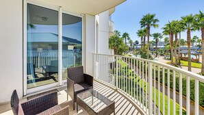 A balcony with wicker furniture, a glass table, and a view of a pool area with palm trees. - Walk to Beaches: Resort Condo in Destin! (Destin)