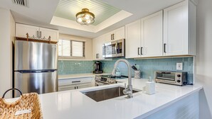 A modern kitchen with white cabinets, stainless steel appliances, a large island with a sink, and a ceiling light fixture. - Walk to Beach & Bites! St Augustine Resort Condo (St. Augustine)
