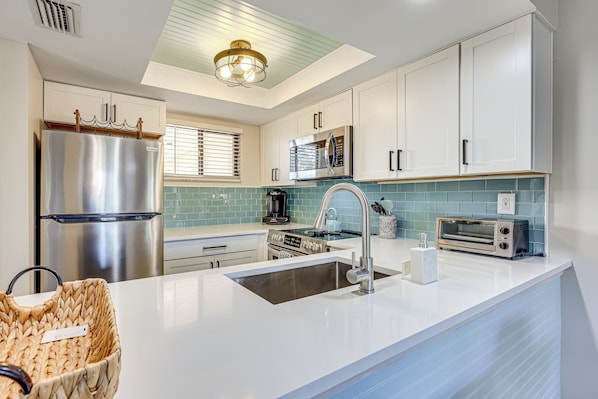A modern kitchen with white cabinets, stainless steel appliances, a large island with a sink, and a ceiling light fixture.