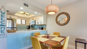 A modern kitchen with white cabinets, a blue countertop, and a central island. There is a dining area with a wooden table and yellow chairs. - Walk to Beach & Bites! St Augustine Resort Condo (St. Augustine)