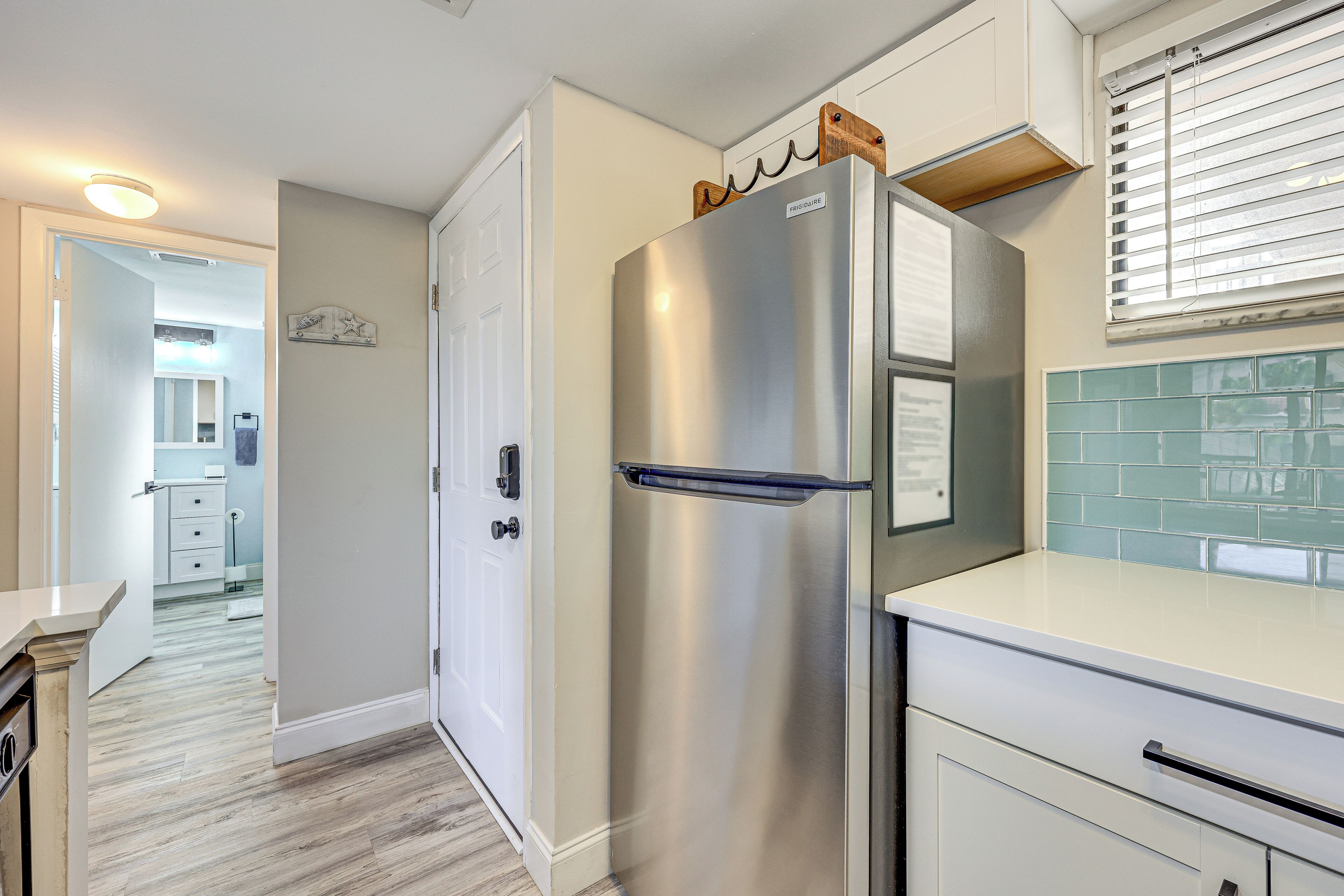 A modern kitchen with a stainless steel refrigerator, white cabinetry, and a tiled backsplash.