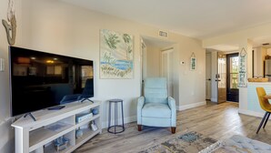 A living room with a flat-screen TV, a light blue armchair, a patterned rug, and a wooden coffee table. - Walk to Beach & Bites! St Augustine Resort Condo (St. Augustine)