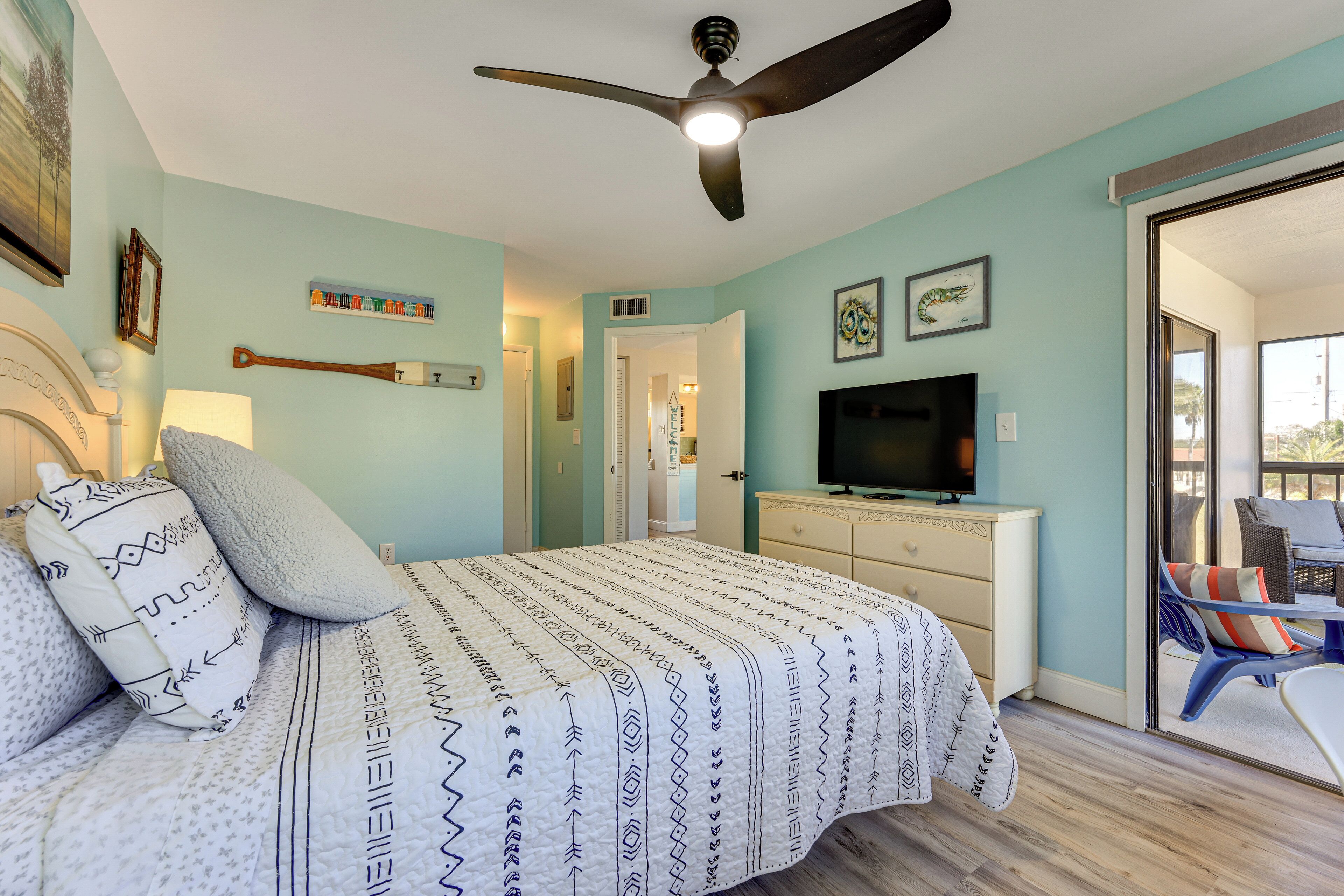 A bedroom with a bed, a ceiling fan, a television, and a view of the outside.
