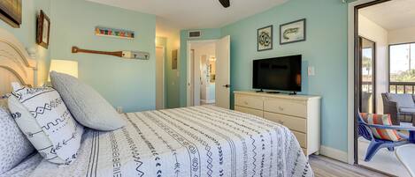A bedroom with a bed, a ceiling fan, a television, and a view of the outside.