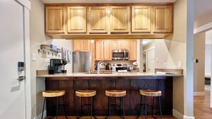 A modern kitchen with wooden cabinets, stainless steel appliances, and a bar area with stools. - Spacious 2 Bdrm, Short walk to lifts! Perfect for a Family! (Mount Crested Butte)