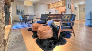 A modern living room with a stone accent wall, a dining area with chairs, a kitchen with wooden cabinets, and a black leather sofa. - Spacious 2 Bdrm, Short walk to lifts! Perfect for a Family! (Mount Crested Butte)