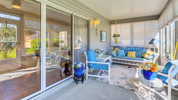 Eine überdachte Terrasse mit Sitzgelegenheit, eine Glastür, die nach draußen führt, und ein kleiner Tisch mit einem blauen Blumentopf.