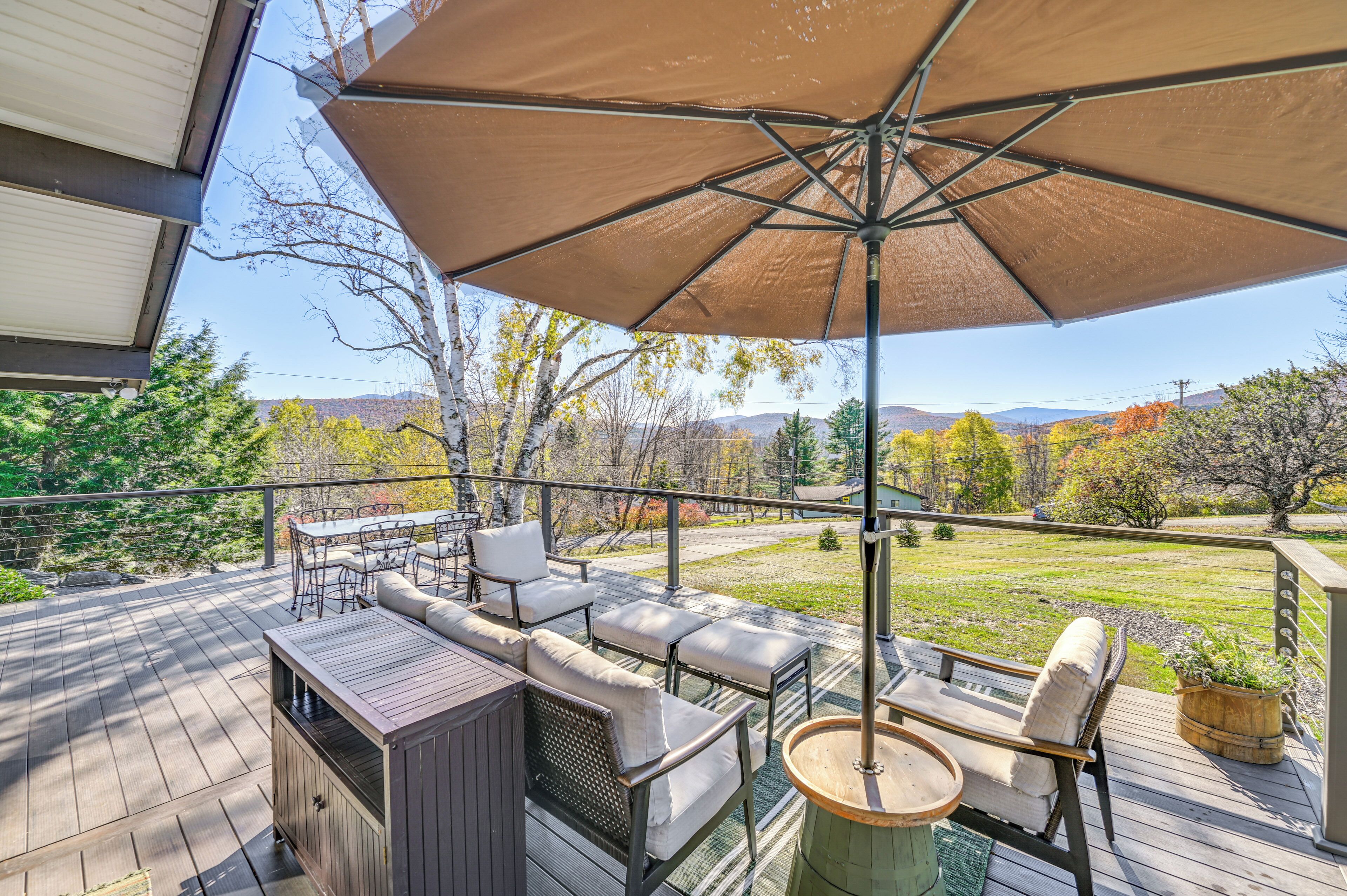 A deck with outdoor furniture, a large umbrella, and a view of a grassy yard and trees.