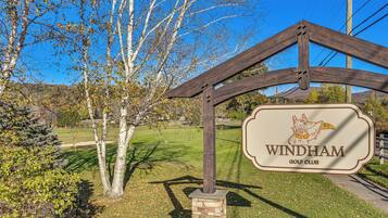 A golf club sign with a logo, surrounded by trees and a clear sky.