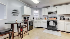 Uma cozinha moderna com armários brancos, fogão preto e mesa de vidro redonda com cadeiras.