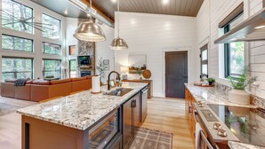 A modern kitchen with a large island, stainless steel appliances, and ample natural light from large windows. - Cozy Secluded Cabin in the Heart of Hochatown (Broken Bow)