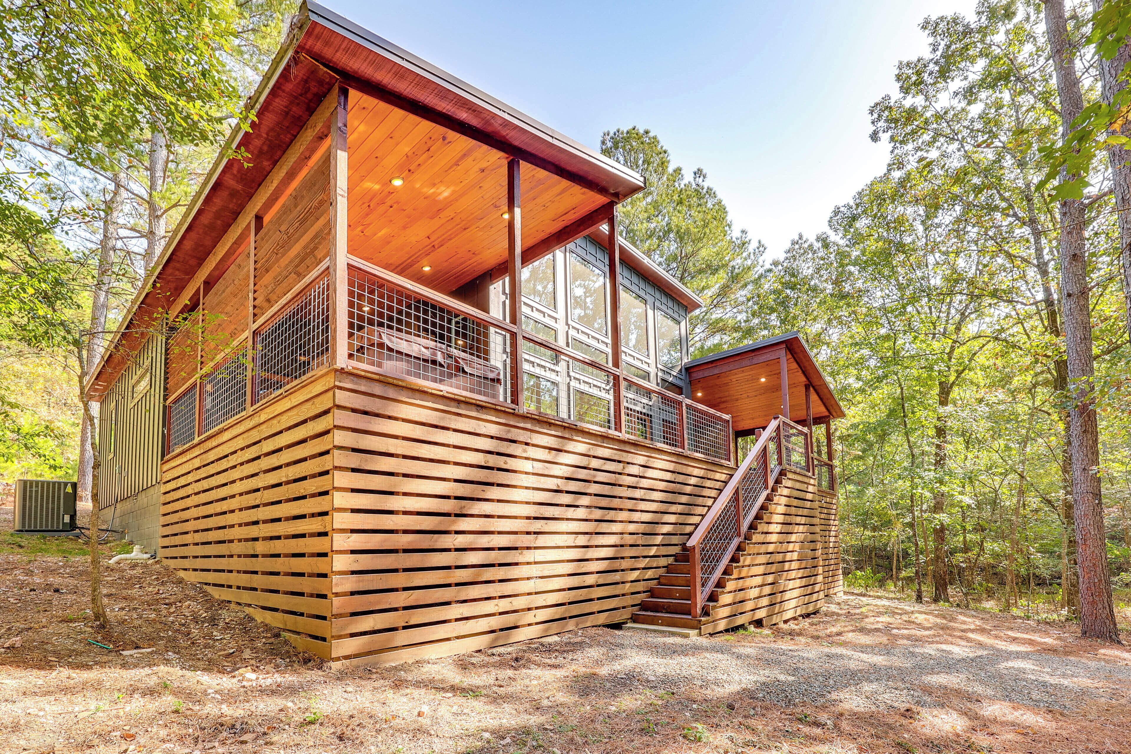 A wooden cabin with a balcony, large windows, and a staircase leading to an upper level.