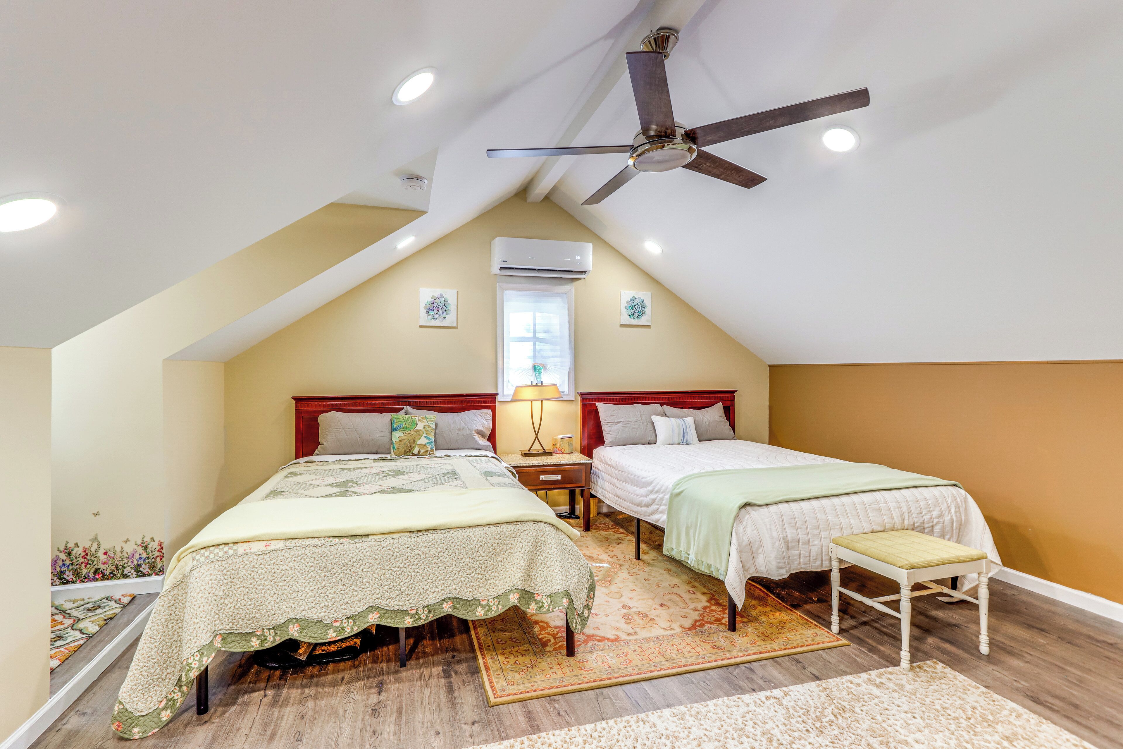 Un dormitorio con dos camas, ventilador de techo, equipo de aire acondicionado y ventana con luz natural.