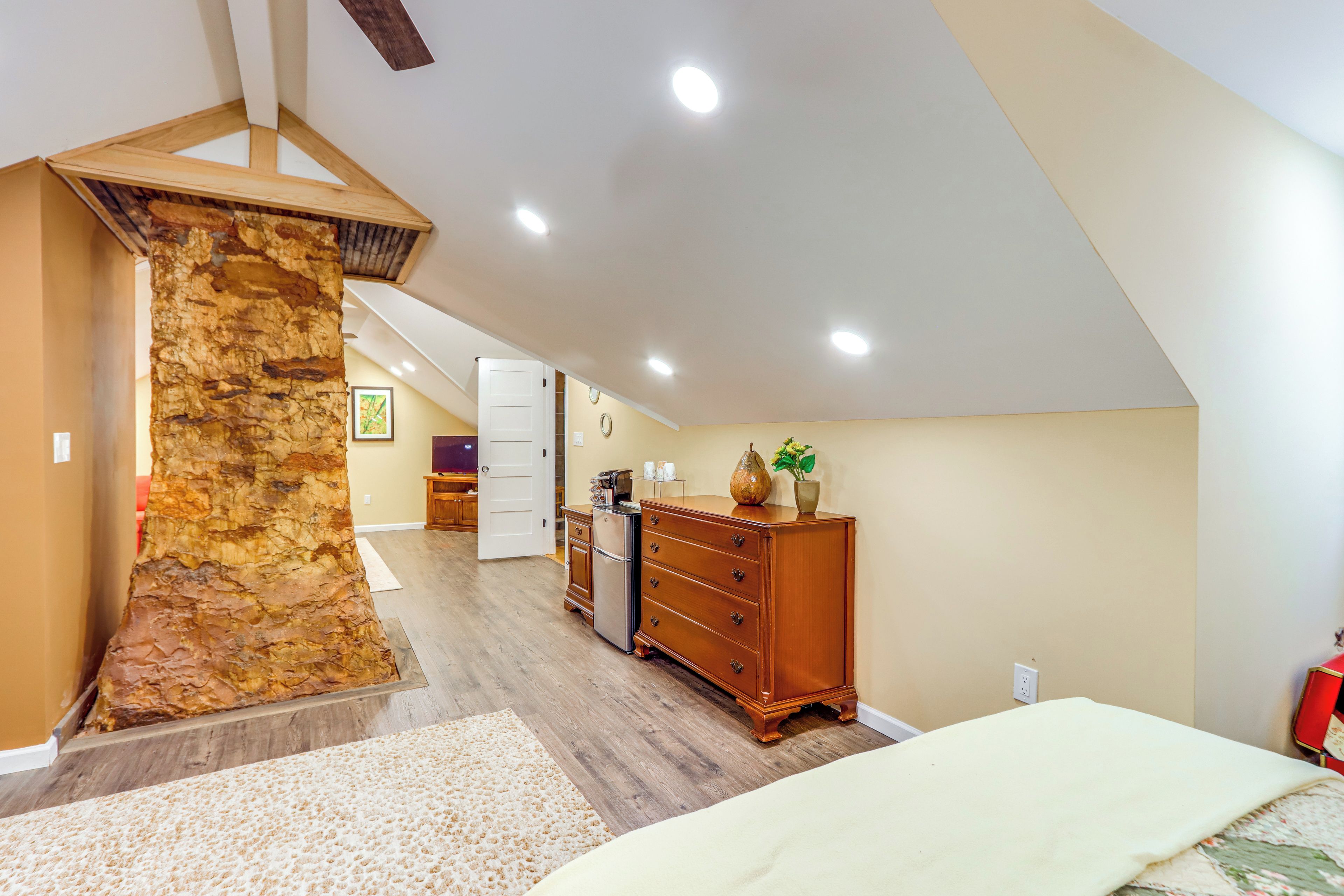 A bedroom with a stone accent wall, wooden dresser, and a bed with a floral bedspread.