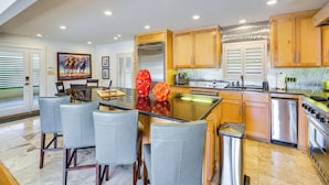 A modern kitchen with a central island, bar stools, stainless steel appliances, and wooden cabinets.