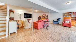 A spacious living room with a wooden floor, a red sofa, a blue armchair, and a bookshelf. - Private Deck: Berkeley Springs Getaway! (Berkeley Springs)