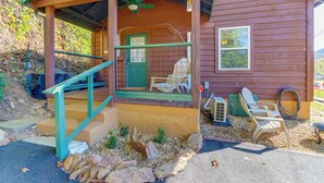 Une cabane en bois avec une véranda, une porte verte et une chaise à l’extérieur.