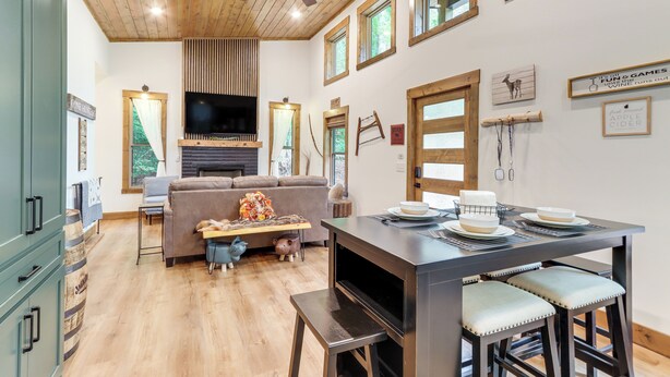 Un vaste espace de vie doté d’un plafond en bois, d’une cheminée, d’un téléviseur et d’une table à manger avec des tabourets de bar.