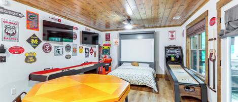 A room with a wooden ceiling, a bed with a patterned bedspread, a table with a yellow tablecloth, and various sports team memorabilia on the walls.