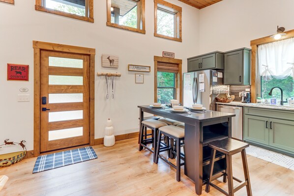 A kitchen with a wooden island, bar stools, a refrigerator, and a window with a view of greenery.