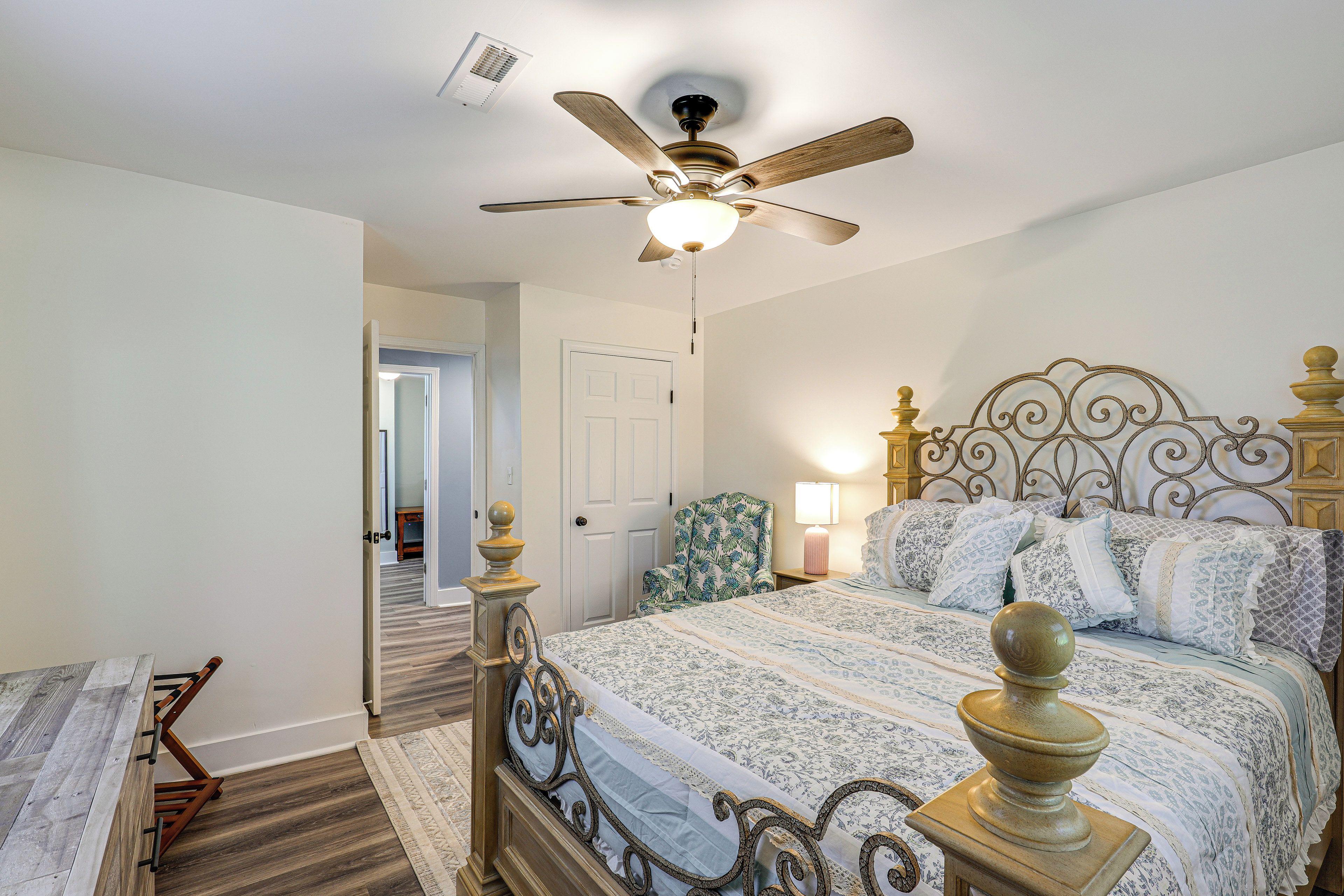 A bedroom with a bed, a ceiling fan, a nightstand, a chair, and a door leading to another room.