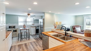 A modern kitchen with a wooden countertop, stainless steel appliances, and a dining area with stools. - Small-town Charm & Local Dining: Home in Burgaw! (Burgaw)