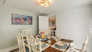 A dining area with a wooden table set for four, surrounded by white chairs. A chandelier hangs from the ceiling, and a colorful painting is on the wall. - Small-town Charm & Local Dining: Home in Burgaw! (Burgaw)