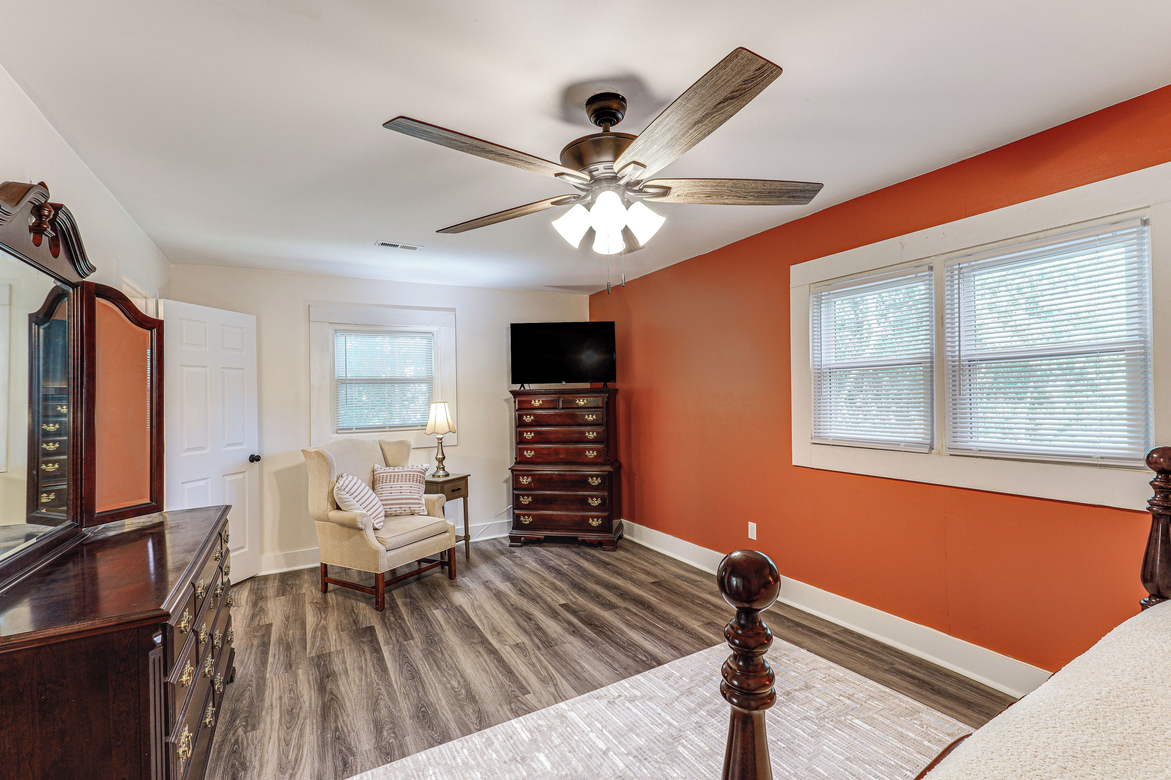 A bedroom with a ceiling fan, a dresser, a chair, a TV, and a window with blinds.