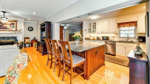 A spacious kitchen with wooden cabinets, a granite countertop, and a dining area with wooden chairs. - 1 Mi to Dtwn: Home w/ Fire Pit & Deck in Hudson! (Hudson)