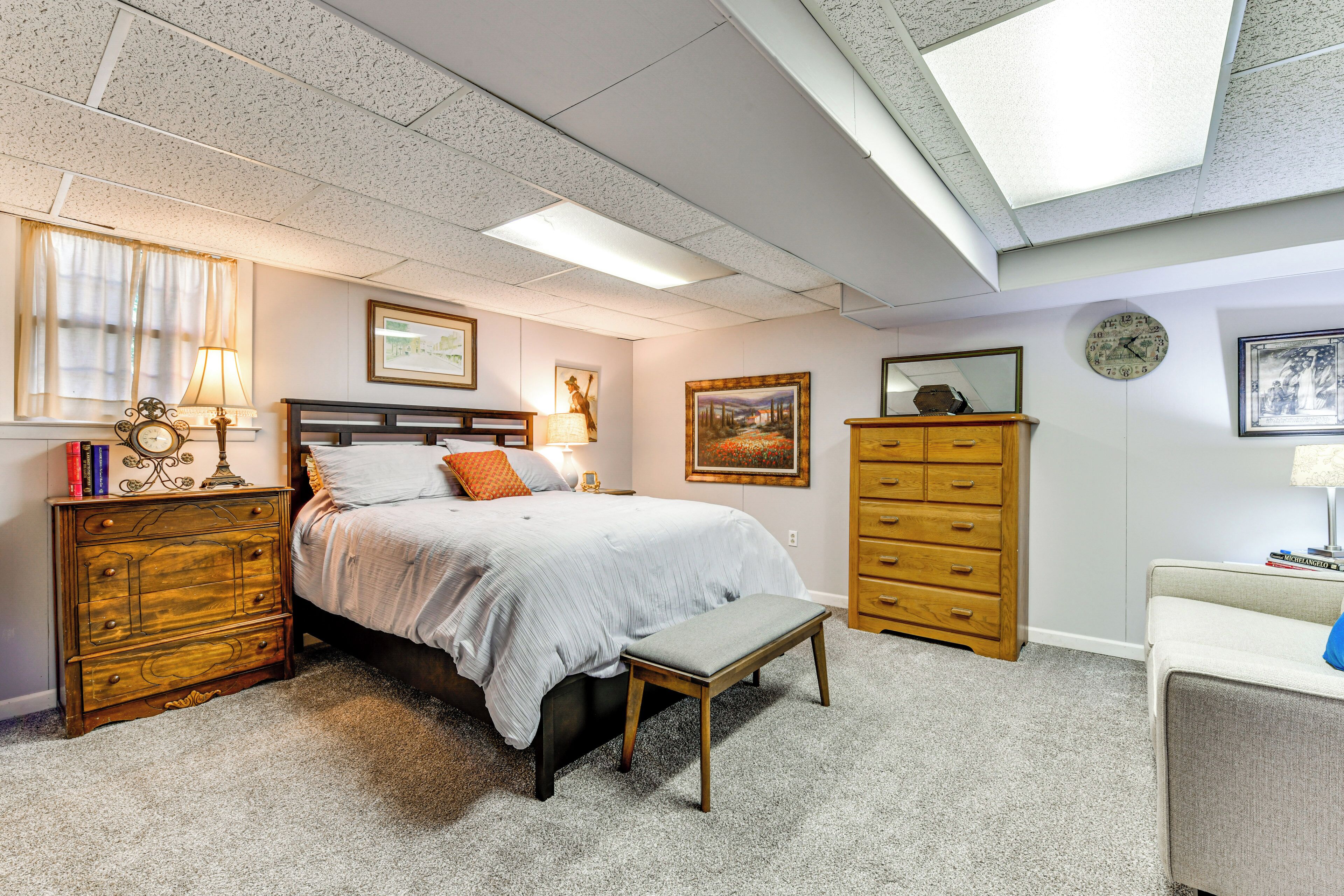 A bedroom with a bed, wooden dresser, bench, and various wall decorations.
